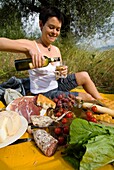 Frau gießt eine Flasche Wein in Vorbereitung auf ein Picknick unter Olivenbäumen ein