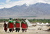 Ladakhische Frauen in traditioneller Kleidung und mit Hüten gehen unter schneebedeckten Bergen spazieren