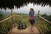 A Backpacker Woman Standing With Her Rucksack On The Balcony Of A Bamboo Hut Overlooking East Khasi Hills