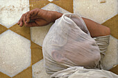 Old Woman In Veil Lying On Tiled Floor