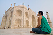 Frau sitzt auf dem Boden und bewundert das Taj Mahal in der Morgendämmerung