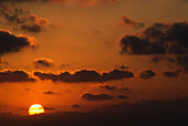 Sonne und Wolken bei Sonnenuntergang in orangefarbenem Himmel