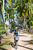 Junge Frau beim Radfahren entlang der Hauptstraße auf der Insel Don Khon.