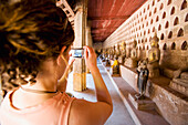 Frau fotografiert im Kreuzgang mit über 2000 silbernen und keramischen Buddhas in kleinen Nischen.