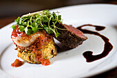 Kobe Beef Tenderloin Roasted And Sliced And Accompanied By Bronzed Alaskan Weathervane Scallop And Served Over A Yukon Gold Potato Cake With Fresh Baby Arugula, Shaved Asiago Cheese, Balsamic Veal Reduction And Roasted Tomato Preserves