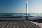 Laternenmast entlang einer Strandpromenade mit blauem Horizont; Malaga, Andalusien, Spanien