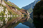 Berge, die sich im Koman-See spiegeln, und ein blauer Himmel; Albanien