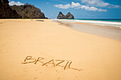 View of morro dos irmaos from praia do bode with brazil written in the sand; Fernando de noronha pernambuco brazil