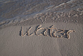 The Word Water Handwritten In The Sand At The Water's Edge; Tulum, Mexico