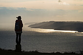 Silhouette einer Frau, die die Aussicht auf Lyme Regis von der Spitze des Golden Cap an der Jurassic Coast bewundert; Seatown, Dorset, England