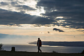 Frau, die in der Nähe der Spitze des Golden Cap mit Lyme Regis dahinter spazieren geht, Jurassic Coast; Dorset, England