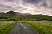 Blick entlang einer Straße am frühen Morgen mit der aufgehenden Sonne hinter dem schwarzen Cuillin-Kamm; Glen Brittle, Skye, Schottland