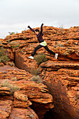 A Tourist Jumps Over A Rugged Rock Formation At Kings Canyon; Northern Territory, Australia