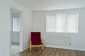 Ein roter Stuhl steht in der Ecke eines weißen Zimmers; London, England