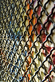 A Chain Link Fence Against A Wall With Colourful Spray Painted Graffiti; Barcelona, Spain
