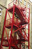 Eine rote Metalltreppe an der Außenseite eines Wohngebäudes, Shoreditch; London, England