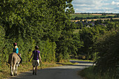 Mother With Girl On Donkey Walking Along A Road; Normandy, France