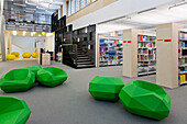 A healthcare college library with open spaces, green chairs and book stacks. A modern light and airy building. 