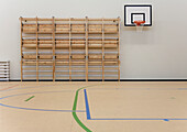 Indoor basketball court at a school. Wooden floor and marked court, a hoop and backboard.