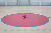 A school sports hall with a marked indoor football pitch, a striped blue and yellow ball in a pink circle. 