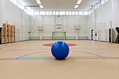 Sportanlagen eines Gymnasiums, eine große Turnhalle mit Sportplätzen, Basketballkörben und einem Tor, ein blauer Ball.