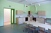 Eine moderne Schule, eine Küche mit Einbauschränken und Öfen, ein langer Tisch mit Stühlen.