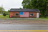 A Sale Today Eine Tafel und eine amerikanische Flagge auf einem leeren Gebäude an einer Straße in einer Kleinstadt.