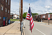 Amerikanische Flagge, die an einem Laternenpfahl auf einer verlassenen Hauptstraße weht.