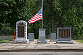 War memorials, inscribed headstones and American flag honoring US war veterans in a graveyard.