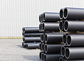 Stacks of industrial PVC pipes piled up outside a manufacturing facility.