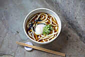 A bowl of noodles, vegetables and broth and a set of chopsticks. 