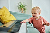 Toddler playing with electronic piano keyboard on sofa