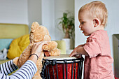 Toddler and teddy bear playing bongo drum together at home