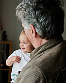 Close up of smiling toddler in arms of grandfather looking out of window