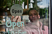 Man placing Open sign in window of shop