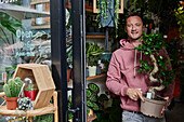 Portrait of man standing in doorway of flower shop holding plant