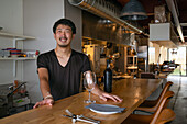 Ein Mann, Besitzer und Manager eines kleinen Restaurants, an einem gedeckten Tisch mit einer offenen Flasche Wein und einem Glas, 