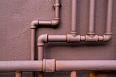 Entlang einer braunen Wand verlaufende Erdgasleitungen, Ventile und Verbindungsstellen.
