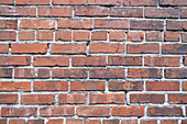 Eine Ziegelmauer aus roten Tonziegeln, die in einem regelmäßigen Muster zu einer Mauer verlegt sind. 