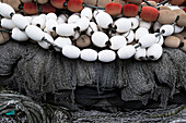 Ein Haufen kommerzieller Fischernetze auf einem Kai, weiße und rote Plastikschwimmer und Netze und Seile. 