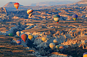 Türkei, Anatolien, Kappadokien, Goreme. Heißluftballons fliegen über Felsformationen und Feldlandschaften im Roten Tal, Goreme-Nationalpark, UNESCO-Welterbestätte.