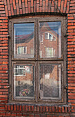 Fenster in einem Reihenhaus in Wislica, Polen, mit Spiegelungen im Haus auf der anderen Straßenseite.