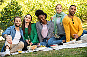 Porträt von lächelnden jungen Freunden beim Picknick im öffentlichen Park