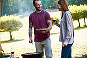 Smiling young couple talking while standing near barbecue grill in park