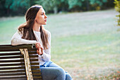 Thoughtful young woman sitting on bench in park
