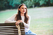 Lächelnde junge Frau sitzt auf einer Bank im Park