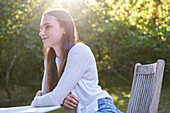 Lächelnde junge Frau auf einem Stuhl im Park sitzend