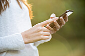 Mittelteil einer jungen Frau, die ein Smartphone im Park benutzt