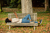 Junge Frau, die auf einer Parkbank liegend ein digitales Tablet benutzt
