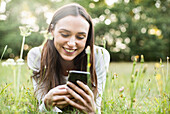Junge Frau, die ihr Smartphone benutzt, während sie im Park liegt